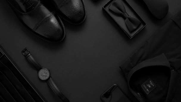 A sophisticated flat lay of black mens fashion accessories, including shoes, tie, shirt, and watch on a dark background. - Footage, Video