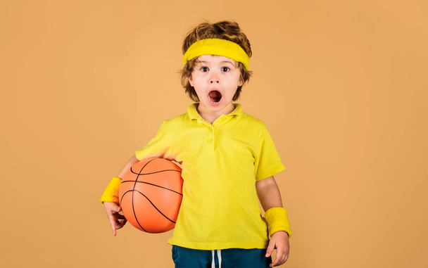 Sport for children. Surprised basketball player boy in sportswear with basketball ball. Fitness, training, healthy lifestyle and hobby sport concept. Little basketballer in sports uniform with ball - Photo, Image