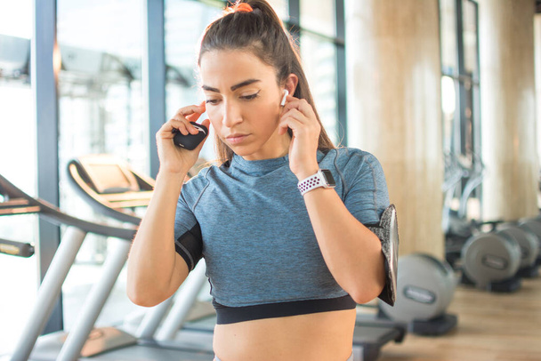 Mujer deportiva con auriculares inalámbricos escuchando música en el gimnasio. - Foto, Imagen