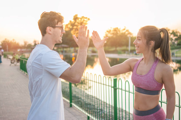 Sportieve jonge fitte vrouw en knappe man geven high five aan elkaar aan het einde van een succesvolle training buiten - Foto, afbeelding
