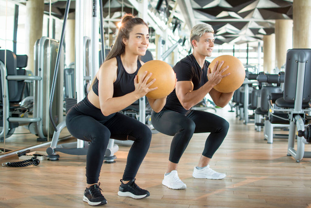 Młoda para fitness w odzieży sportowej ćwiczy pilates ball na siłowni. Sportowy mężczyzna i kobieta trening razem w klubie zdrowia. - Zdjęcie, obraz