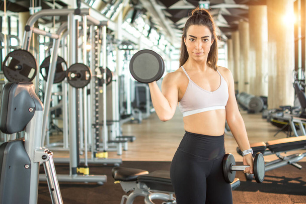 Retrato en forma de mujer deportiva haciendo ejercicio con pesas en el gimnasio. - Foto, imagen