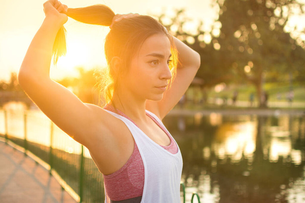 Woman tying hair in ponytail getting ready for exercising outdoors at sunset - Photo, Image