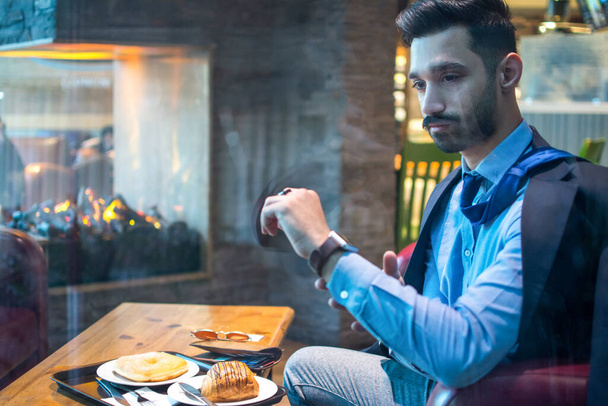 Hombre de negocios mirando el reloj mientras está sentado en la cafetería. A través de la vista - Foto, imagen