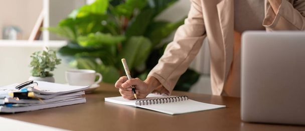 Gros plan des mains avec stylo de jeune femme d'affaires est assis à table avec ordinateur portable tout en prenant des notes, l'analyse des informations. - Photo, image