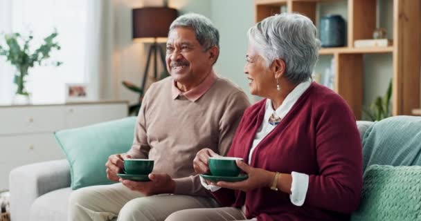 Oudere echtpaar, gelukkig en koffie op de bank in huis, huis en woonkamer voor pensionering. Mensen, oudere partners en familie die thee drinken, lachen en ontspannen op de bank voor liefde, verbondenheid en genegenheid. - Video