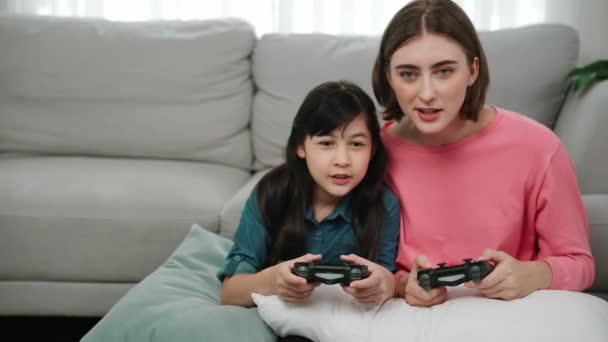 Happy mom and energetic girl playing game and spending time together. Caucasian mother sitting near her child while hold joystick and focus on playing game with daughter at cozy living room. Pedagogy. - Footage, Video