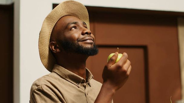 Afro-Amerikaanse man ruikt lokaal geteelde appels in de supermarkt, ondersteunt niet vervuilende kleine bedrijven door het kopen van bio-voedsel. Klant die fruit uit kratten kiest, geniet van een natuurlijk aroma. Camera 1. - Foto, afbeelding