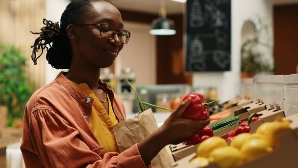 Vegan γυναίκα που παίρνει τα τοπικά καλλιεργούμενα λαχανικά από κιβώτια, πηγαίνει για ψώνια στην τοπική αγορά αγροτών. Τακτικός πελάτης επιλέγει πολύχρωμα ώριμα προϊόντα, μη ρυπογόνες γεωργικές επιχειρήσεις. Κάμερα 1. - Φωτογραφία, εικόνα