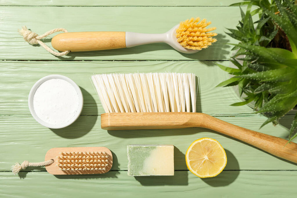 Cepillos, jabón, limón, soda en cuenco y planta sobre fondo de madera verde, vista superior - Foto, Imagen