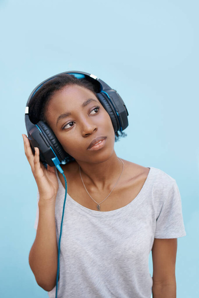 Thinking, music and black woman with headphones in city for sound, track or listening to podcast on blue background. Streaming, earphones or gen z student outdoor with radio, playlist or audio ebook. - Photo, Image