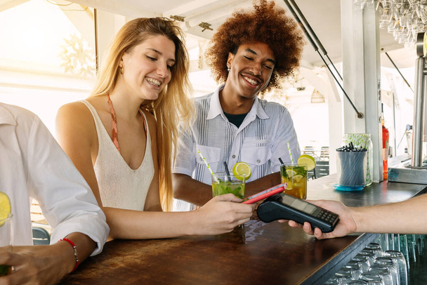 Casal jovem usando cartão de crédito ou débito sem contato para pagamento no bar da praia - Foto, Imagem