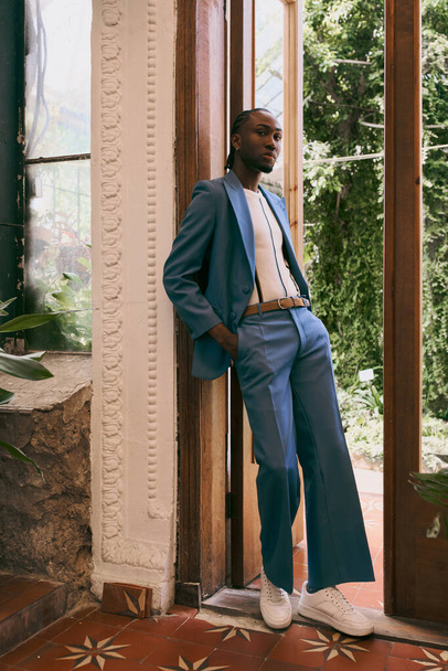 Jóképű afro-amerikai férfi kék öltönyben, egy élénk zöld kerti ajtónak támaszkodva.. - Fotó, kép