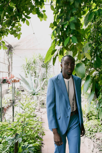 Un bel homme afro-américain en costume bleu se tient au milieu d'un jardin vert vif. - Photo, image