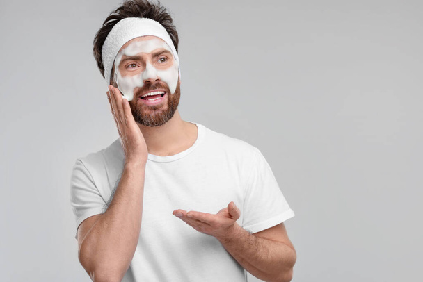 Man with headband washing his face on light grey background, space for text - Fotoğraf, Görsel