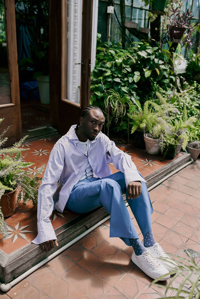 Красивый афроамериканец сидит на скамейке перед яркими зелеными растениями. - Фото, изображение