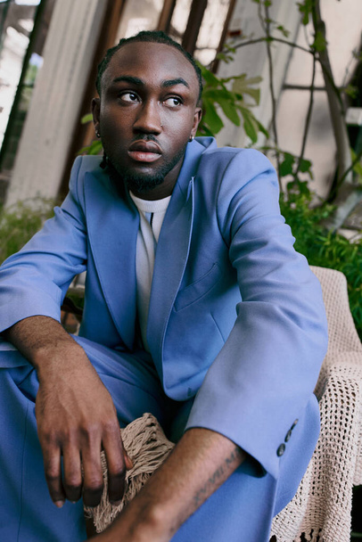 鮮やかな緑の庭に椅子に座っている青いスーツのスタイリッシュなアフリカ系アメリカ人男性. - 写真・画像