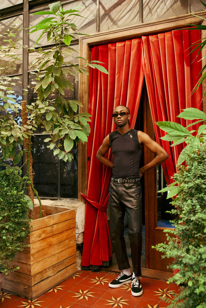 Ein gutaussehender afroamerikanischer Mann steht selbstbewusst vor einem leuchtend roten Vorhang. - Foto, Bild