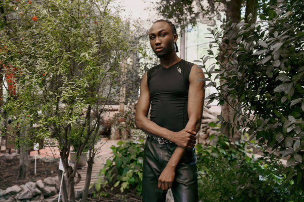 Przystojny Afroamerykanin z wyrafinowanym eleganckim stylem stojący pewnie w zielonym ogrodzie. - Zdjęcie, obraz