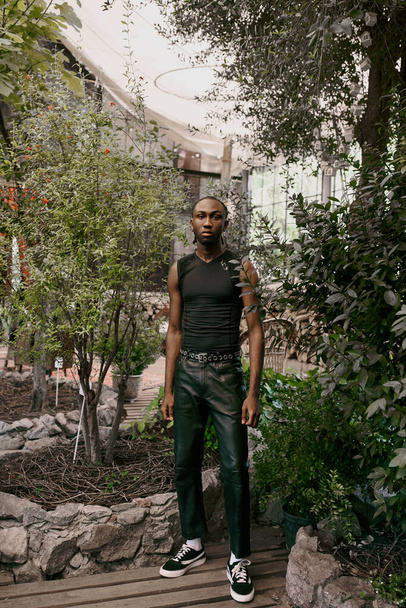 Ένας όμορφος Αφροαμερικάνος με εκλεπτυσμένο στυλ, στέκεται σε έναν καταπράσινο κήπο.. - Φωτογραφία, εικόνα