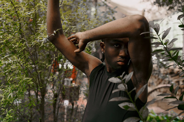 Un homme afro-américain sophistiqué se tient près d'un arbre, les mains sur la tête. - Photo, image