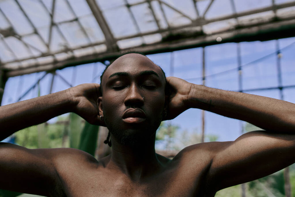 Bel homme afro-américain dans le style dapper, torse nu, tenant les oreilles dans un jardin vert vif. - Photo, image
