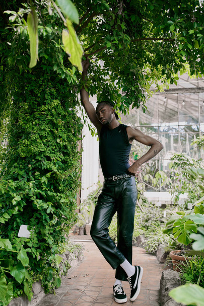Um homem afro-americano sofisticado de traje preto em pé graciosamente sob uma árvore verde exuberante. - Foto, Imagem