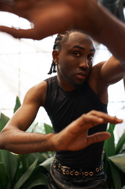 Стильний афроамериканський чоловік у чорній сорочці в яскравому зеленому саду. - Фото, зображення