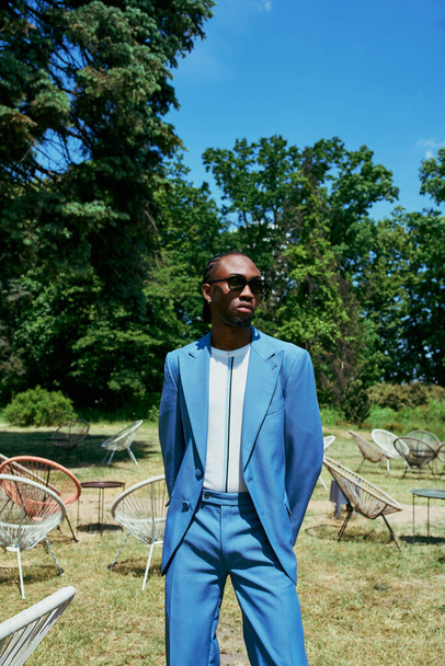 Un hombre afroamericano sofisticado con un traje azul se encuentra gentilmente en un campo vibrante. - Foto, imagen