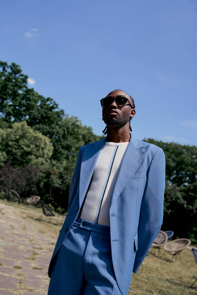 Afrikai amerikai férfi kék öltönyben és napszemüvegben pózol a buja zöld kertben.. - Fotó, kép