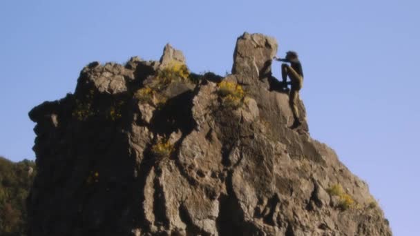 Ein Bergsteiger steht siegreich auf dem schroffen Gipfel, die Arme jubelnd in den klaren Himmel gereckt. Diese filmische Aufnahme, aufgenommen mit einer hochwertigen Blackmagic-Kamera, friert den Moment des Triumphes ein - Filmmaterial, Video