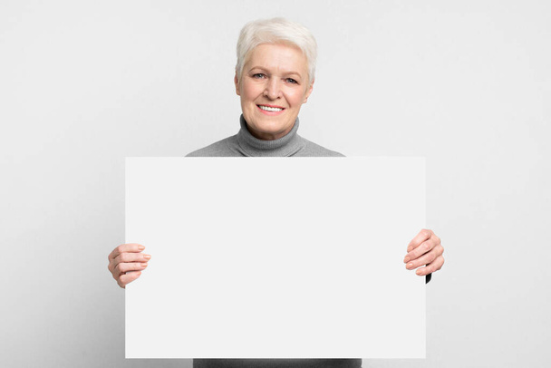 Das Bild zeigt eine ältere europäische Frau mit einem leeren Schild, ideal für benutzerdefinierte Nachrichten innerhalb eines s3niorlife-Rahmens - Foto, Bild