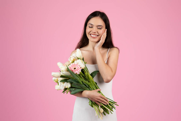 笑顔の若い女性は,ヨーロッパの夏の新鮮さの感覚を伝えるチューリップの美しい花束を保持しています. ピンクで孤立したZ世代代表 - 写真・画像
