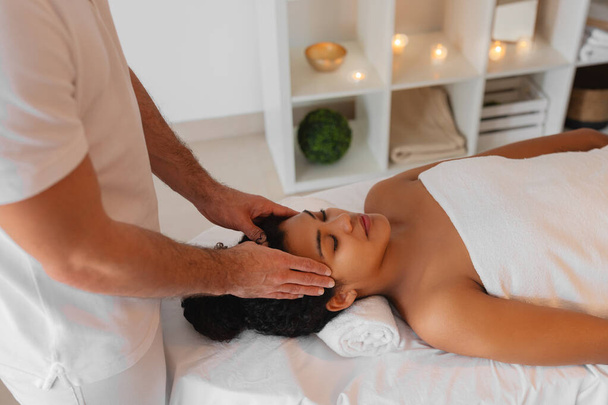 Образ крупным планом обратите внимание на лицо афроамериканской женщины, когда она получает успокаивающий массаж головы в спа-центре - Фото, изображение