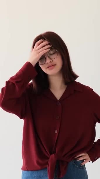 Depressed Caucasian teenage girl showing facepalm gesture on white background. Emotional stress or failure reaction concept. Vertical video. - Footage, Video
