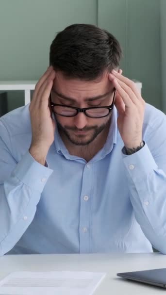 疲れた男性の白人フリーランサーは,オフィスの文書を扱う頭痛を抱えています. 痛みによる苦しみ。 バーンアウトコンセプト。 バーティカルビデオ. - 映像、動画