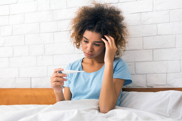 Jeune femme malade avec fièvre vérifiant sa température avec un thermomètre à la maison - Photo, image