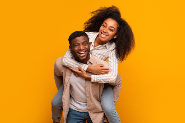Neşeli Afrikalı Amerikalı çift sarılıp gülüyor sarı bir stüdyoda - Fotoğraf, Görsel