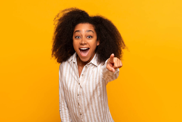 Feliz jovem afro-americana com cabelo encaracolado apontando para a câmera, fundo brilhantemente colorido - Foto, Imagem