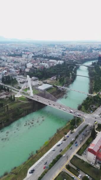 Nyaralás és utazás koncepció. Podgorica Montenegró: Gyönyörű naplemente a belváros felett, beleértve a Moraca folyót és a Millennium hidat, a híres mérföldkövet. Légi felvétel. - Felvétel, videó