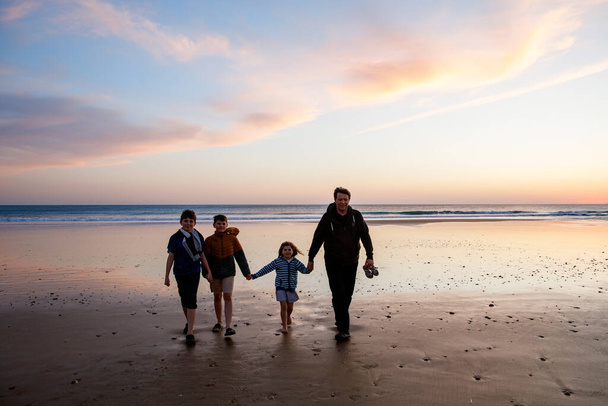 Portré három gyerekről és apa boldog gyerekeiről apával a parton naplementekor. Boldog család, ember, két iskolás fiú és egy óvodás lány. A testvérek jól érzik magukat együtt. Kötődés. - Fotó, kép