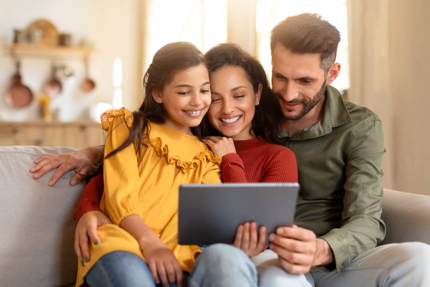 Uma família encantada de três pessoas está envolvida com um tablet digital no sofá, imerso em tecnologia em conjunto - Foto, Imagem