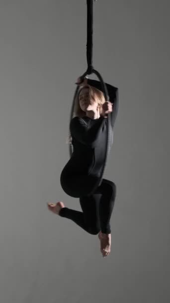 Biała kobieta profesjonalna tancerka akrobatyczna wykonująca pokaz tańca latającego na wiszącej antenowej obręczy nad szarym tłem. Pionowe wideo. - Materiał filmowy, wideo