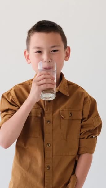 Ευτυχισμένος και χαρούμενος Ασιάτης νεαρός μαθητής πίνει νερό από γυαλί σε λευκό φόντο. Αναζωογόνηση, αναγέννηση, έννοια αναζωογόνησης. Κάθετη βίντεο. - Πλάνα, βίντεο