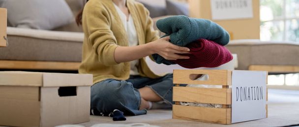 Spende, asiatische junge Frau sitzt Pack-Objekt zu Hause, legt Sachen in Spendenbox mit Second-Hand-Kleidung, Charity-Hilfe und bedürftigen Menschen. Recycling wiederverwerten. - Foto, Bild
