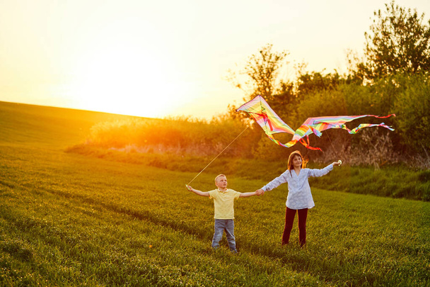 Gelukkige kinderen lanceren een vlieger in het veld bij zonsondergang. Kleine jongen en meisje op zomervakantie. - Foto, afbeelding