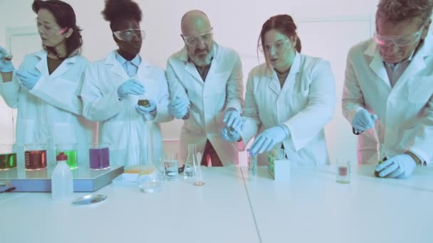 Gerichte wetenschappers voeren een chemisch experiment uit met kleurrijke vloeistoffen in een modern laboratorium - Video