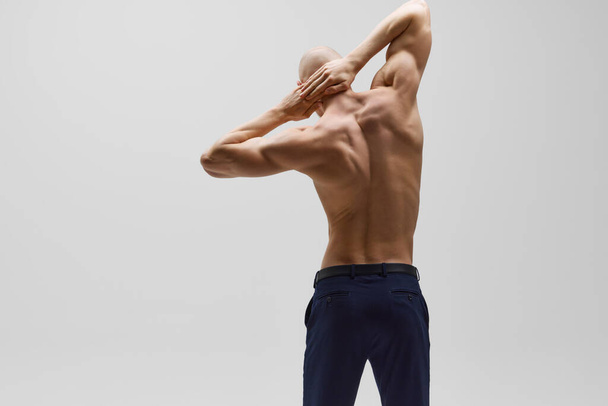Homme athlétique posant les mains derrière le dos et montrant sa posture saine et son dos musclé sur fond gris. Concept de santé des hommes, l'auto-soin, la mode et la beauté, mode de vie saine. Publicité - Photo, image
