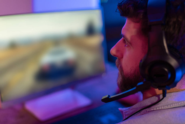 Een gerichte man gamer met hoofdtelefoon is het spelen van een racespel, de presentatie van de meeslepende ervaring van moderne gaming - Foto, afbeelding