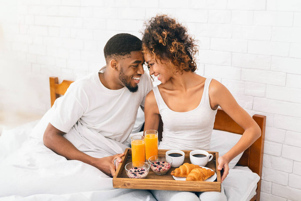 Счастливая африканско-американская пара влюблена наслаждаясь завтраком в постели, прекрасное утро - Фото, изображение